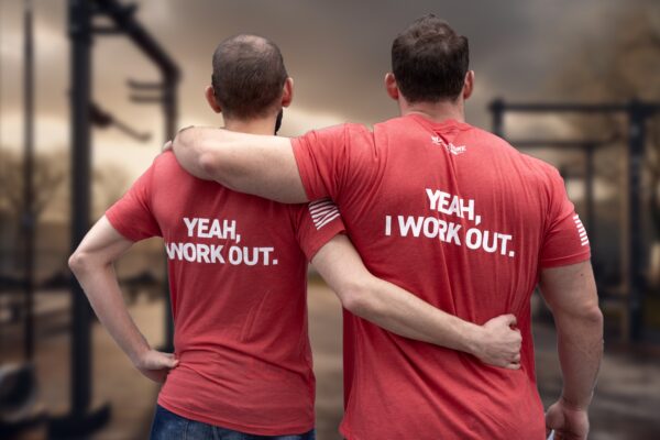 Two Models with arms around each other wearing "Yeah, I Work Out" shirt. Blurred gym background.
